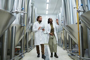 Smiling Black female brewer showing brewing equipment to inspector - Powered by Adobe