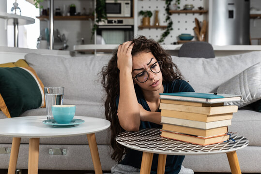 Young college woman law student frustrated with pile of books she need to read and study for exam. Future lawyer girl feeling anxious and nervous before exam. Education concept