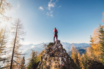 On top of the world - Caucasian woman hiker standing on a rock, admiring the view of autumn mountains in the distance