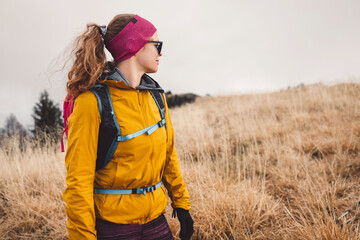 Waist up woman hiker in yellow jacket and pink headband up in the mountains on a foggy autumn day