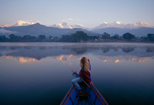 A woman in a rowboat gazes at the Annapurna Range at dawn.; Annapurna Range, Himalaya Mountains, Nepal.