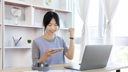 Asian woman playing games on mobile phone having fun, Play games on the sofa in the living room on weekends, Resting at home, Comfort zone, Touch screen mobile phone.