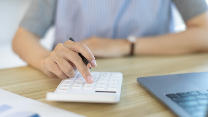 Fototapeta premium Businesswoman presses a calculator to calculate earnings and analyze company earnings in his private office, Information in finance and accounting, Company performance and revenue.