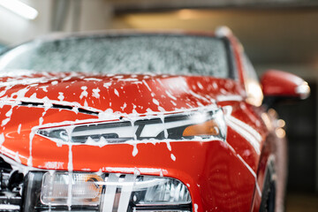 Washing a car headlight at auto wash service. Soapy red car. Washing of crossover car with active...