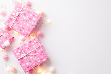 Valentine's Day concept. Top view photo of pink gift boxes in wrapping paper with heart pattern light bulb garland and fluffy pompons on isolated white background with empty space