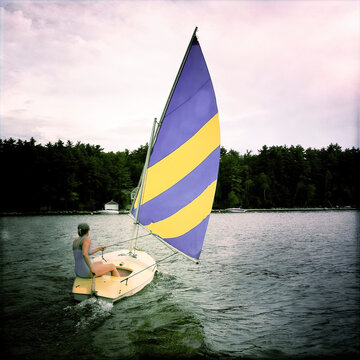 A woman sails a small boat across Sebago Lake.; Sebago Lake, Maine.