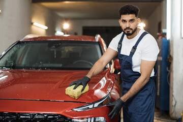 Car washing and detailing concept. Young concentrated bearded male worker holding the sponge in...