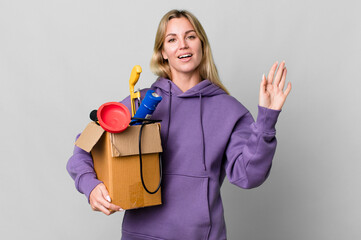 caucasian blonde woman smiling happily, waving hand, welcoming and greeting you. housekeeper concept