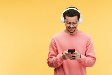 Happy guy in headphones, eyeglasses and pink sweatshirt scrolling through playlist or online audio...
