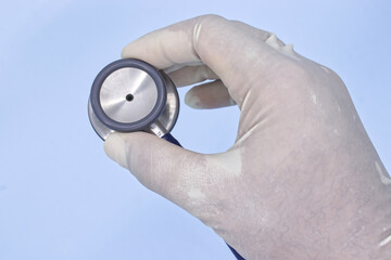 Hand with medical glove holding stethoscope on blue background