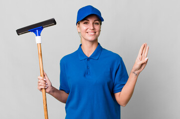 caucasian blonde woman smiling and looking friendly, showing number three. windows washer concept