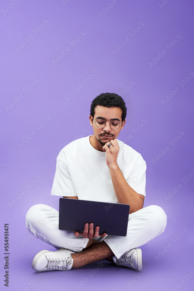 Poster young serious man with laptop on his knees watching online video or working over new business projec