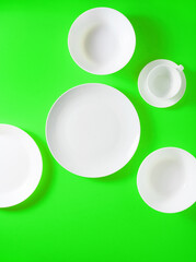 a set of white dishes on a bright green background. taken from above