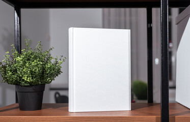 Paper book in hard cover mockup on wood shelf, house plant in modern loft office interior. Business literature ad