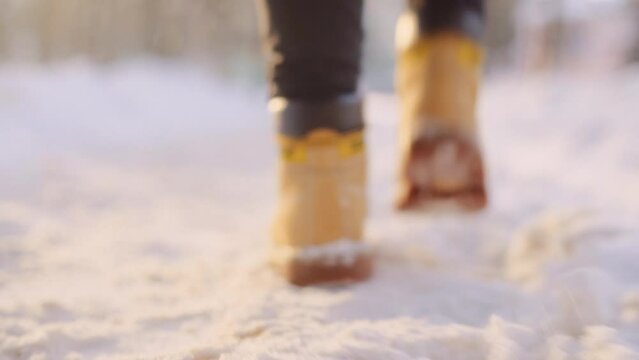Walking on a snow-covered path in winter. Foot following in yellow boots close up