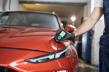 Closeup view of male hand, using film coating thickness gauge device to check car paint. Auto...