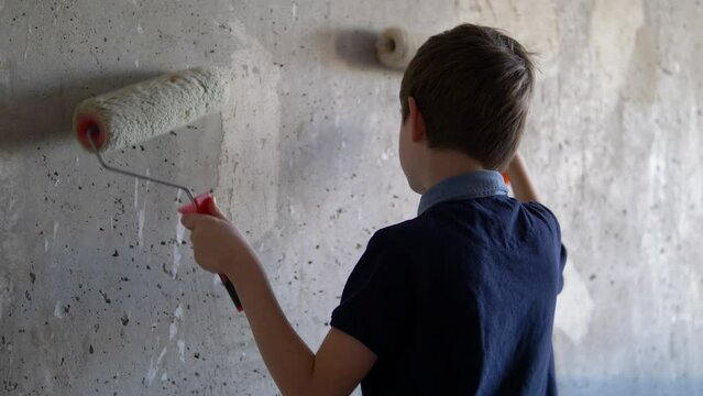 caucasian boy 8-9 years old with paint rollers paints the walls repairing the apartment, children help to make repairs in the house. child learns to work with a construction tool