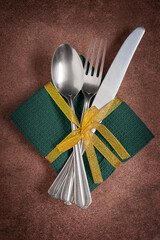 Top view of set of tableware units such as silver metal spoon, fork and knife on green textile...