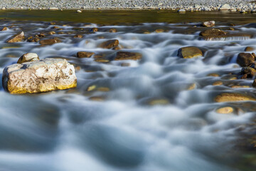 Obraz na płótnie Canvas Long exposure time. Long exposure on the river, Long exposure of the river in the Caucasus mountains. The stones in the river are blurred from long exposure. Stones in the riverbed in the mountains.