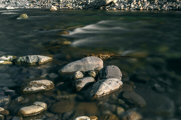 A long exposure on the river flowing through the rocks. Stones in the riverbed in the mountains. Water flowing over rocks. Long exposure time. A long exposition of the river in the Caucasus mountains.
