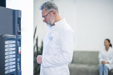 Fototapeta premium Gray-haired mature doctor standing near the slot machine