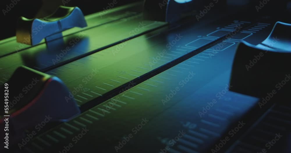Poster close-up pan over individual faders of audio mixer in colorful pulsating light of party