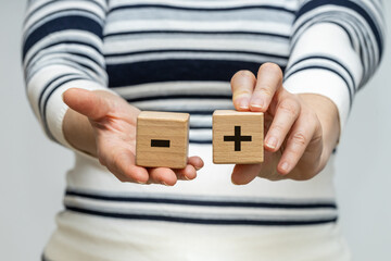 Pros and cons, A woman holds wooden blocks with a positive and negative symbol in her hands, the concept of pros and cons, ups and downs - obrazy, fototapety, plakaty