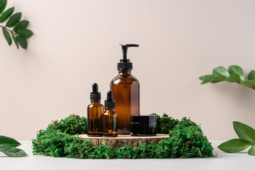 Dark glass cosmetic bottles on wooden podium surrounded by green moss. Mockup for beauty organic...