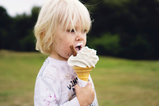 Dirty blonde boy eating an ice cream.