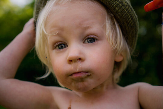 Boy with hat on and snotty nose looking into the camera.