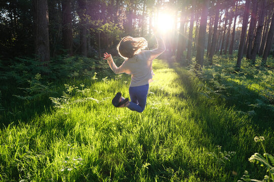 A young girl jumping for joy in a sunlit forest.