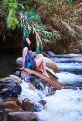 latin mid adult woman sitting on a stone in the Cochiguaz river with eyes closed enjoying the climate and nature of the Valle del Elqui, Cochiguaz