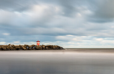 Meeresk&uuml;ste mit Hafenlichtturm und bew&ouml;lktem Himmel