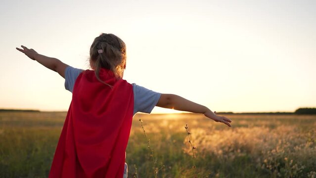 Dream of freedom. Girl superhero in park at sunset. Child winner hero plays in nature. An active girl in red superhero costume runs in park.Childhood dream of victory and heroism.Happy family concept