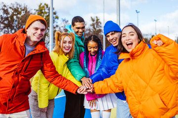 Multiracial group of young happy friends wearing colorful winter jackets meeting outdoors in...