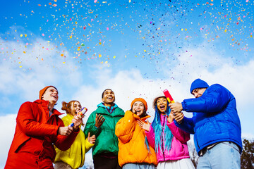 Multiracial group of young happy friends meeting outdoors in winter and celebrating party with colorful confetti, concepts about youth and event celebration