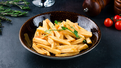 Fried french fries in bowl with rosemary and cherry tomatoes on table.