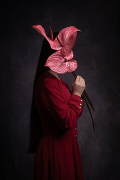 abstract dark portrait of a woman in a red dress holding pink anthurium flowers hiding her face