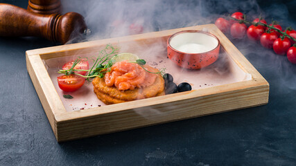 Potato pancakes with salmon fish, cherry tomatoes, olives, lime and sour cream.