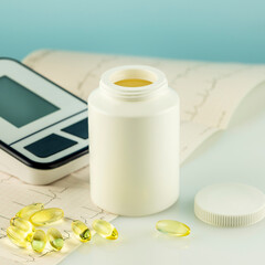 Mockup of natural vitamins or supplements, cardiogram and tonometer on doctor desk. White bottle with healthy supplements in gel capsules. Omega 3. Vitamins and nutrients for heart