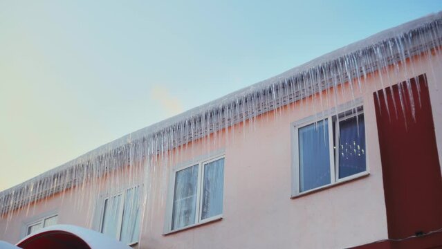 Large icicles hang from the overhang of the roof of the building. Falling ice- winter hazard for passersby