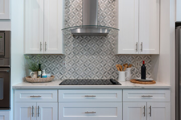 Modern kitchen details of electric stovetop with intricate tile backsplash and sleek white...