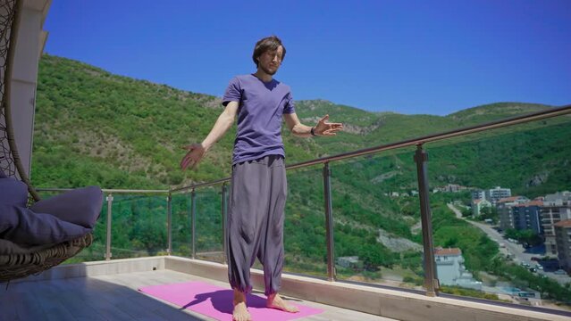 Young man is practicing yoga on in modern apartment terace with mountains and sea in the background
