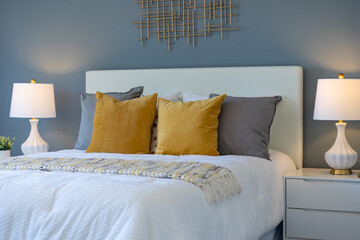 Relaxing bedroom scene of bed with white linens, yellow and violet pillows, side lamps and blue painted wall.