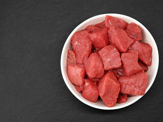 raw diced beef meat in white bowl on black slate background, top view