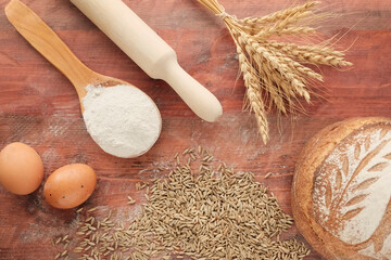 Wheat ears, sack with grain on a wooden light background. Round whole grain bread. Rolling pin, eggs, flour - ingredients for making bread. The concept of farming, natural products.