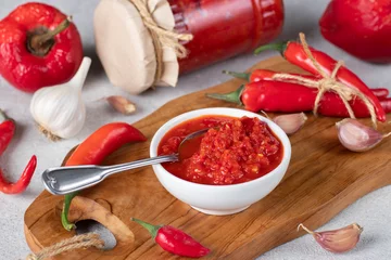 Fotobehang Traditional sauce adjika with hot chili pepper, paste harissa in white bowl on wooden board. Closeup © Anzhela
