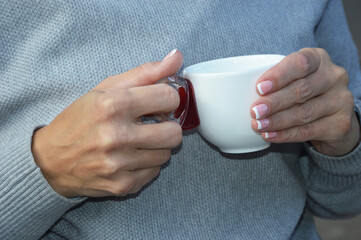 A girl in a gray sweater holds a cup of tea or coffee in her hands.