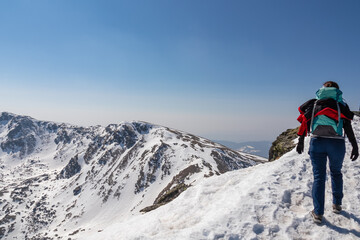 Rear view of woman with backpack hiking on snow covered hiking trail with panoramic view on snow capped mountain peak Zirbitzkogel and Kreiskogel, Seetal Alps, Styria (Steiermark), Austria, Europe