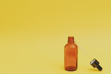 Facial serum in a glass brown bottle on a yellow background, cosmetics commercial shoot